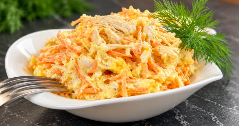 Салат із куркою, морквою по-корейськи, яйцями та плавленим сиром у білій мисці, прикрашений кропом.